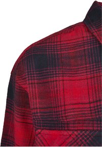 Rød og sort ternet flannel skjorte med skulder og øvre bryst synlige samt krave på hvid baggrund