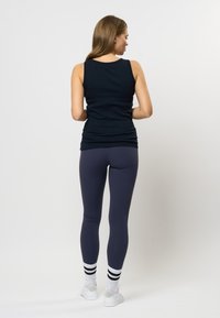 Marinblå ribbad linne i kombination med mörka leggings. Vita sneakers med svarta randiga strumpor. Slät tyg och åtsittande design.