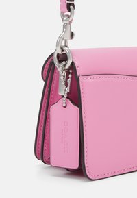 Coin d’un sac à main en cuir rose avec garniture en argent et une étiquette Coach en cuir rose assortie suspendue à une chaîne.