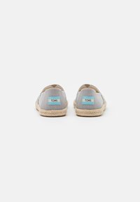 Espadrilles en toile gris clair avec une semelle en jute. Patch du logo TOMS teinté de bleu sur le talon, design arrondi. Silhouette simple et plate.