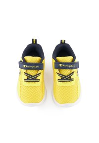 Zapatos deportivos amarillos con parte superior de malla texturizada, acentos en navy y una correa de gancho y bucle. Presenta cordones y una suela blanca.