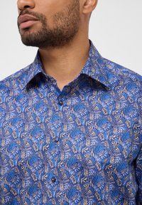 Korte mouwen overhemd in het blauw met een bladpatroon. Heeft een kraag, knoopsluiting en een zachte textuur. Gemaakt van lichte stof.