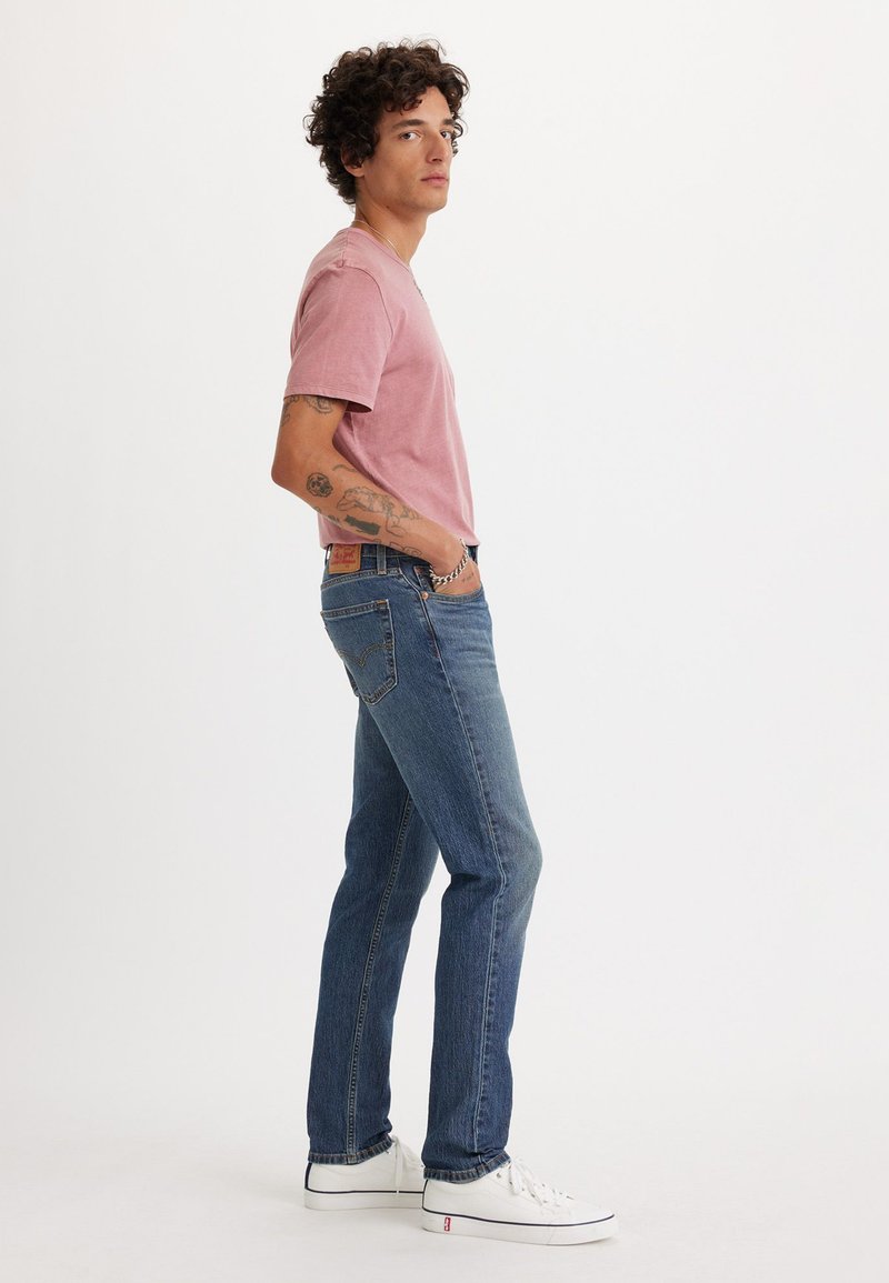 Maglietta rosa a maniche corte, jeans blu e sneaker bianche basse. La maglietta ha una vestibilità comoda; i jeans sono a gamba dritta con un effetto sbiadito.