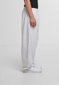 Gray, cotton sweatpants with elastic waistband and side pockets, tapered fit, paired with white sneakers.