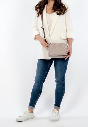 Torba na ramię z miękkiego materiału w odcieniu taupe z diamentowym wzorem, zamek błyskawiczny i brązowy pasek. Połączona z białą marynarką i niebieskimi dżinsami.
