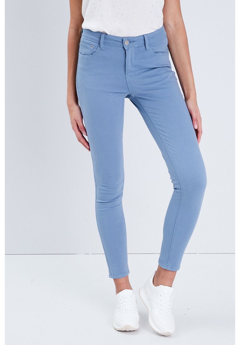 Lyseblå, strækbare skinny jeans med mellemhøj talje, forlommer og en glat tekstur, parret med hvide sneakers.