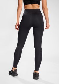 Svarta leggings med hög midja, tillverkade av elastiskt tyg, med en slät yta och en figurnära design.
