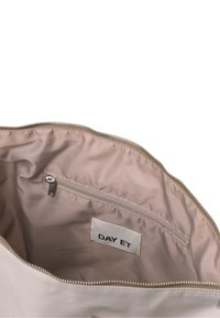 Wnętrze beżowej torby z tkaniny z zamkniętą kieszonką i metką z napisem "DAY ET". Gładka tekstura i złoty detal zamka.