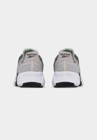 Ζεύγος γκρι και λευκών παπουτσιών Reebok, φωτογραφημένα από πίσω, με δίχτυ ψηλά, ετικέτα με το λογότυπο στον αστράγαλο και μαύρη σόλα με ανάγλυφη επιφάνεια.