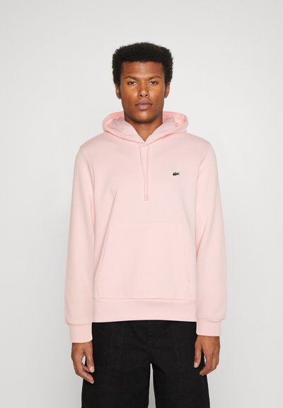 Hoodie rose clair en tissu doux, avec une poche kangourou à l'avant, une capuche avec cordon de serrage réglable, et un logo brodé sur le côté gauche de la poitrine.