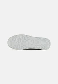 White rubber shoe sole with textured pattern, featuring a star-like design at the center and circular grooves radiating outward.