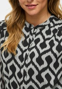 Camicia a maniche lunghe bianca e nera con un motivo geometrico ondulato, caratterizzata da una trama morbida e un colletto.