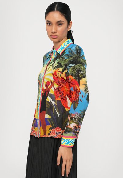 Chemise à boutons colorée avec un imprimé tropical comprenant des feuilles de palmier, des fleurs et des silhouettes. Le col présente un accent à motif vif.