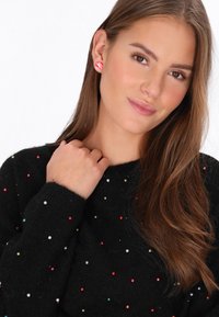 Maglione nero con decorazioni multicolori, caratterizzato da perline rotonde e lucenti. La modella indossa orecchini a strisce rosse. Capelli lunghi e mossi.