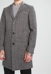 Grå hundetandsmønstret frakke med revers, tre knapper og skræddersyet pasform. Fremstillet af struktureret stof. Lodrette striber under.