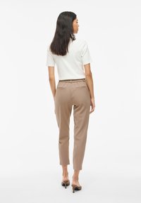 Beige dressade byxor med resårmidja, två bakfickor och en tapered ben-design. Parat med en vit kortärmad topp.