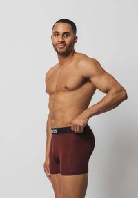 Bordeauxrote Boxershorts mit einem schwarzen elastischen Bund, auf dem "STOCKS" steht. Der Stoff wirkt weich, eng anliegend und leicht. Das Modell ist oberkörperfrei.