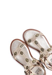 Metalen zilveren sandalen met bruine zolen, voorzien van decoratieve ronde messing accenten en gevlochten banden. Gladde textuur en open teen ontwerp.