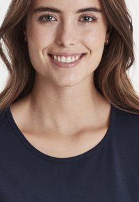 Marineblå top med rund hals fremstillet af glat stof, med et simpelt design uden mønstre. Synlig syning ved halsudskæringen.