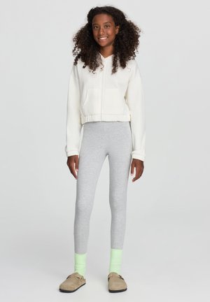 Hoodie bianco corto, leggings grigi, accenti di calze verde neon e scarpe slip-on beige, caratterizzati da una texture morbida e un design casual.