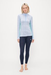 Lyseblå langermet topp med halv-glidelås og blomsterdesign, sammen med marineblå leggings med et lite gjentagende mønster og logo.