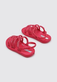 Sandalias de color rosa brillante hechas de caucho duradero, con múltiples correas cruzadas y una suela texturizada para mayor agarre. Incluyen una correa ajustable en el tobillo.