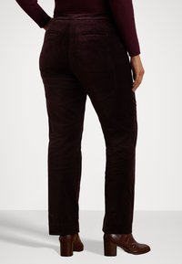 Bordo zomšos kelnės ar tiesia piešimo dizainu, su galiniais kišenėmis ir lygaus paviršiaus, derinamos su rudos spalvos aukštakulniais batais.