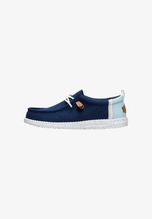 Zapato náutico azul marino con talón azul claro, suela moteada blanca, cordones blancos y detalle en cuero marrón claro en el lateral y en la lengüeta trasera.