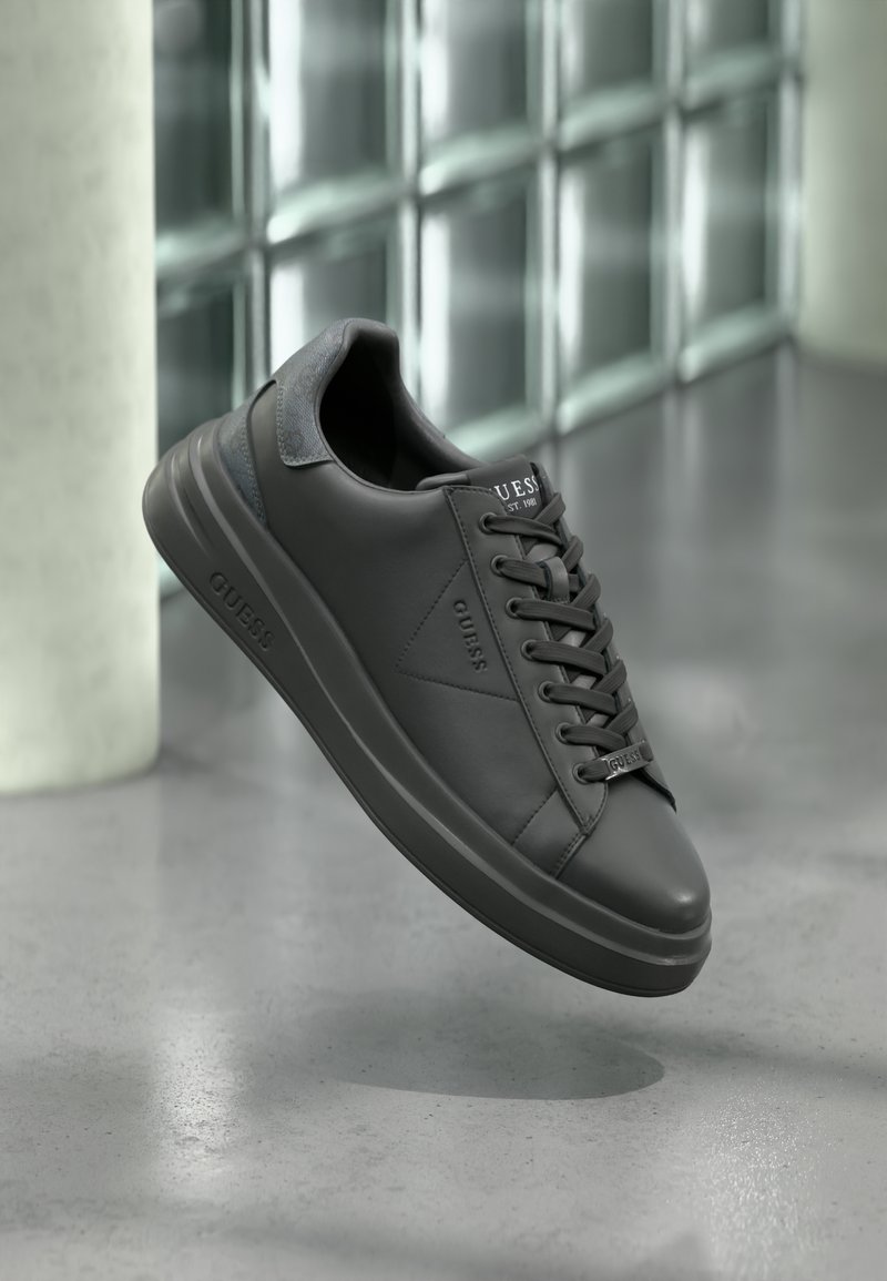 Black leather sneakers with textured accents and a smooth finish. Features a rounded toe, thick sole, and flat laces. Logo displayed on tongue.