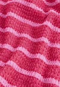 Tekstureret stof i nuancer af rød med skiftevis lyserøde striber, der har en rynket overflade, der tilføjer dybde og dimension.