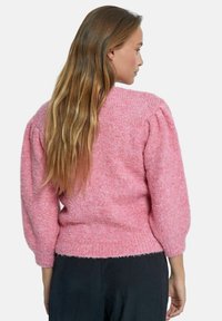 Rosa gestrickter Pullover mit strukturiertem Stoff, Puffärmeln und geripptem Saum, Ansicht von hinten. Das Model trägt schwarze Hosen.