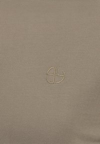 Tessuto beige con una trama liscia, caratterizzato da un piccolo logo ricamato di una tonalità leggermente più chiara. Il design è semplice e minimalista.