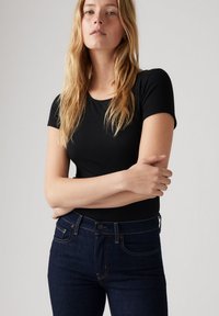 Top negro de manga corta con textura acanalada combinado con unos jeans de mezclilla azul oscuro de corte ajustado, con costuras sutiles y bolsillos frontales.