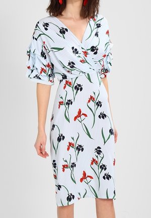 Robe portefeuille bleu clair avec imprimé floral rouge et noir, manches bouffantes jusqu'au coude avec détails à volants, portée par une personne debout.