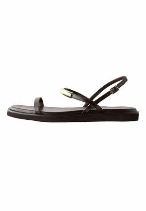 Plokščia tamsiai ruda sandalė su plonais dirželiais, auksine sagtimi ties čiurna ir auksiniu akcentu ant priekinio dirželio.