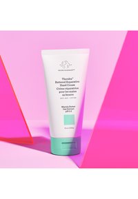 White tube of Drunk Elephant Therablu™ Buttered Reparative Hand Cream with mint-green accents, displayed on a pink background. 75 ml size.
