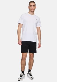 Vit bomull t-shirt med korta ärmar, prydd med en liten svart logo. Matchad med svarta shorts och sportiga vita sneakers med svarta detaljer.