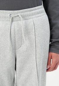 Pantalones de chándal gris claro hechos de una tela suave, con una cinturilla elástica con cordón y bolsillos laterales. Textura suave, diseño sencillo.