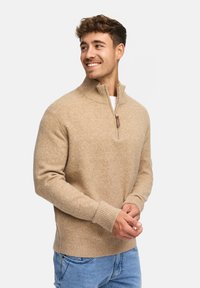 Beiger Strickpullover mit hohem Kragen und halbem Reißverschluss, ausgestattet mit gerippten Bündchen und Saum, aus einem weichen, strukturierten Stoff gefertigt.