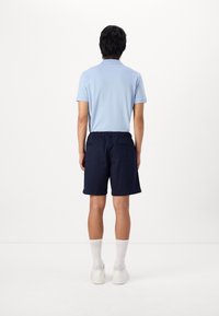 Polo shirt bleu clair pour homme associé à un short à taille élastique bleu marine. Des baskets et des chaussettes blanches complètent la tenue. Design simple, sans motifs.