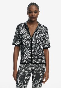 Short-sleeve black and white patterned shirt with a button closure and contrasting black trim, paired with matching patterned pants.