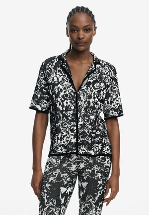 Short-sleeve black and white patterned shirt with a button closure and contrasting black trim, paired with matching patterned pants.