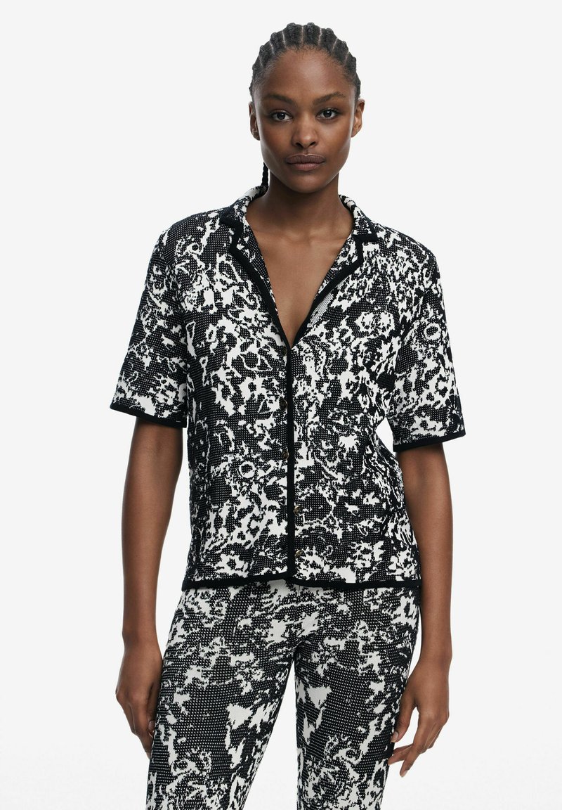 Short-sleeve black and white patterned shirt with a button closure and contrasting black trim, paired with matching patterned pants.