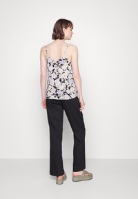 Camisola de alças finas com estampa floral, apresentando um fundo preto com flores roxas claras e brancas. Combinada com calças largas pretas.