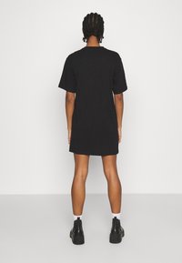 Robe t-shirt noire oversize avec des manches courtes, ourlet droit et texture en coton doux. Portée avec des bottines et des chaussettes blanches.