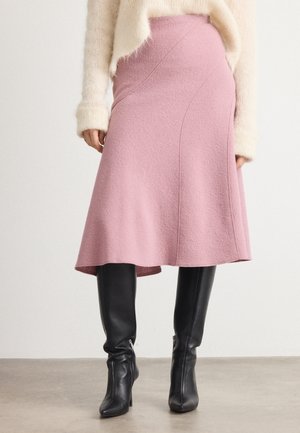 Woman wearing a pink A-line wool skirt, cream fuzzy sweater, and black knee-high leather boots standing on concrete floor.