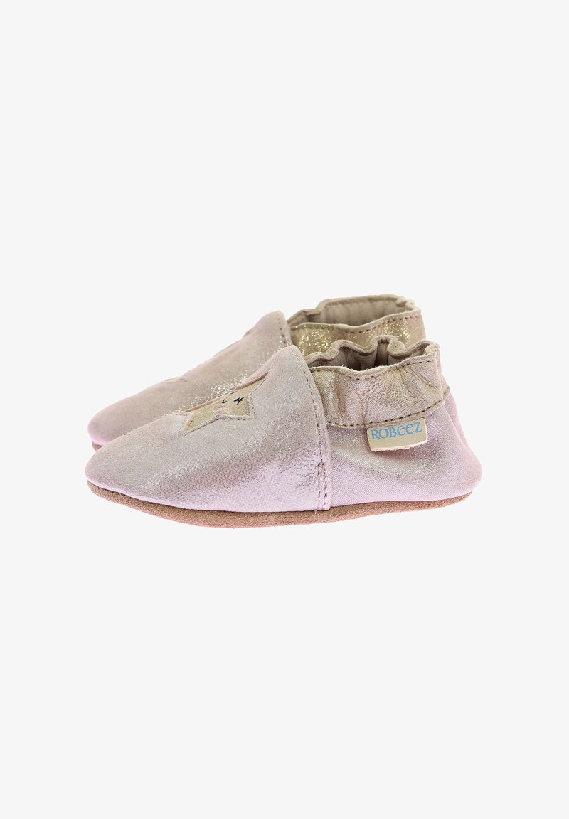 Chaussons pour bébé en suède rose doux avec un détail étoile dorée, une cheville élastique et une semelle texturée ; étiquette de marque sur le côté.