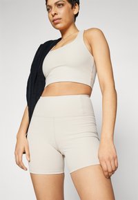 Beige ribbet sportsklærsett som består av en crop top og høy midje shortser, laget av elastisk stoff med en glatt tekstur.