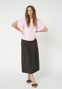 Blusa a righe rosa con maniche a sbuffo, abbinata a una gonna nera di media lunghezza e sandali marroni decorati con un fiocco, su sfondo bianco.