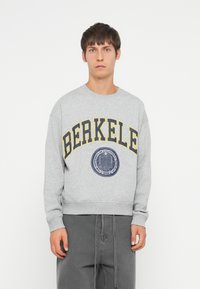 Gray sweatshirt with yellow letters spelling "BERKELE" and a navy emblem. Features ribbed cuffs and waistband, with a relaxed fit.